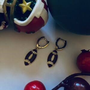 May include: A pair of gold hoop earrings with a black enamel football charm. The football charm has white diamond accents.