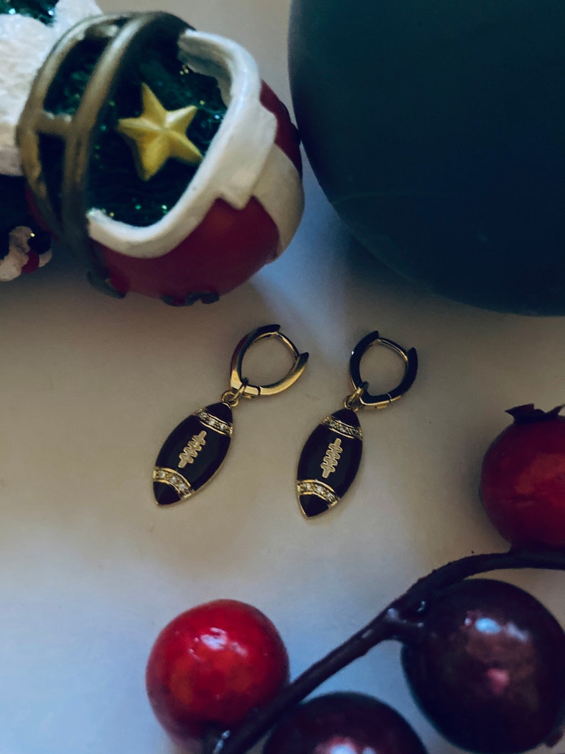 May include: A pair of gold hoop earrings with a black enamel football charm. The football charm has white diamond accents.