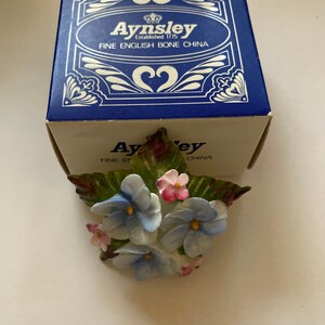 May include: A blue and white porcelain flower bouquet with green leaves. The bouquet is in a box that says "Aysnley Established 1775 Fine English Bone China".