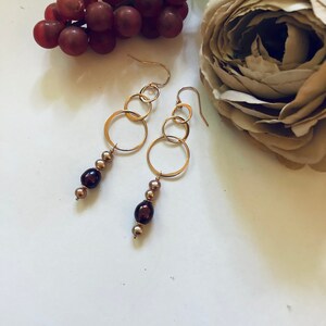 May include: Gold hoop earrings with a dangling chain of brown and gold beads.
