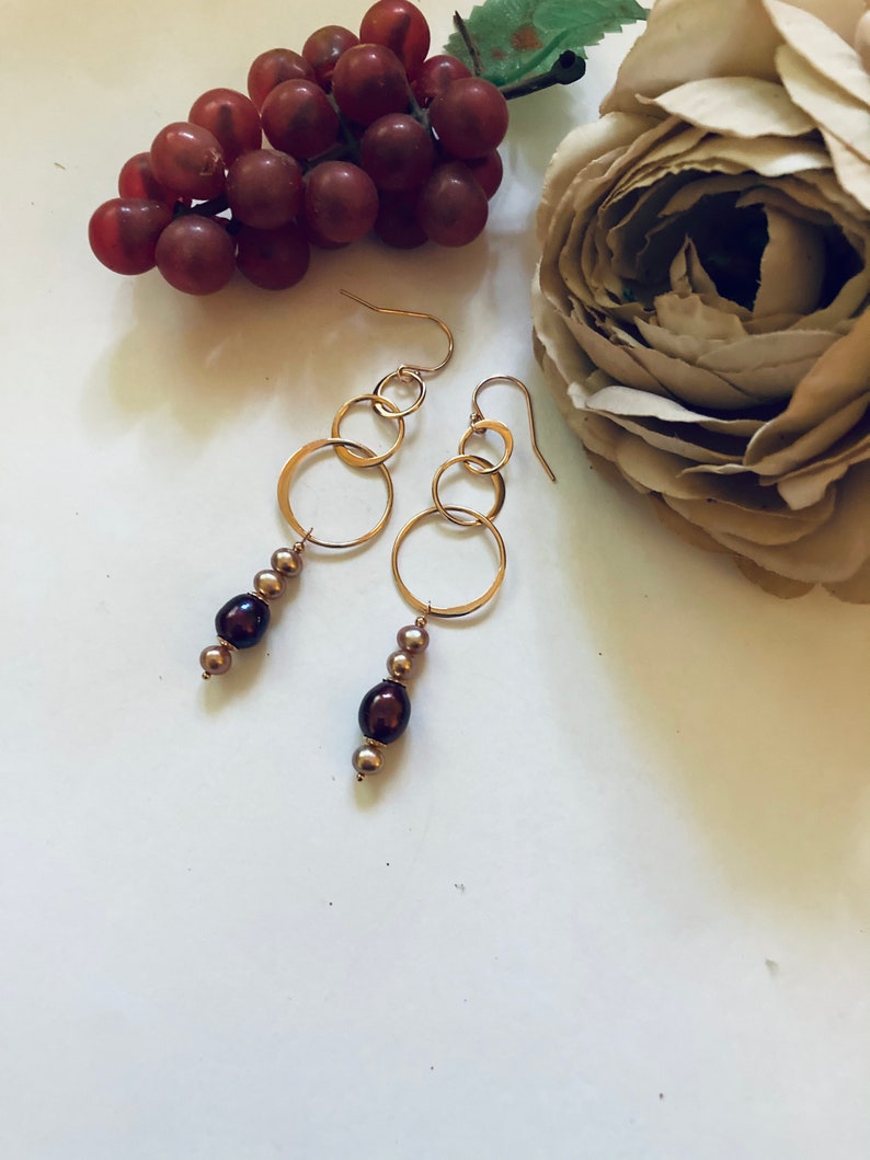 May include: Gold hoop earrings with a dangling chain of brown and gold beads.