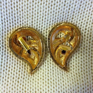 May include: A pair of gold-tone teardrop-shaped earrings with a floral design. The earrings have a clip-on closure.