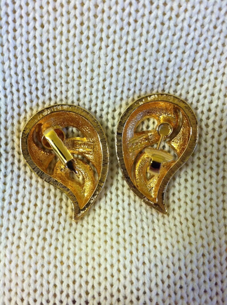 May include: A pair of gold-tone teardrop-shaped earrings with a floral design. The earrings have a clip-on closure.