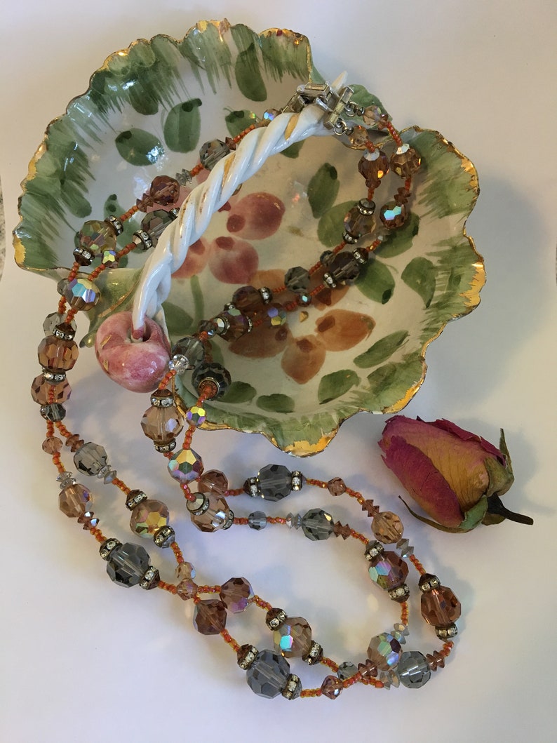 May include: A double strand necklace with brown and gray iridescent beads in a ceramic dish with a floral design.