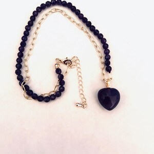 May include: A gold chain necklace with a dark purple heart pendant. The chain is made of small, round beads.