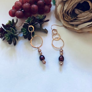 May include: Gold hoop earrings with three connected hoops and a dangling strand of brown and gold pearls.