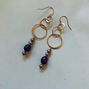 May include: Gold hoop earrings with a dangling chain of small gold circles and brown pearls.