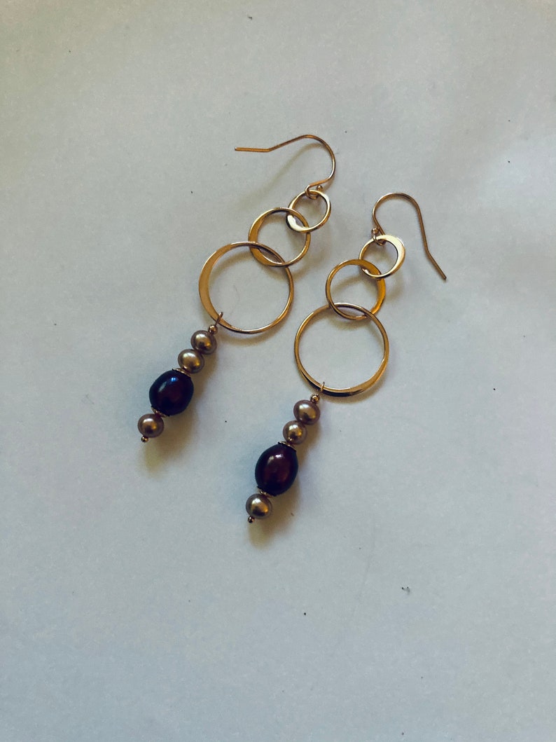 May include: Gold hoop earrings with a dangling chain of small gold circles and brown pearls.