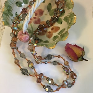 May include: A multi-strand necklace with brown, gray, and clear iridescent beads. The necklace features a pink, round bead in the center.