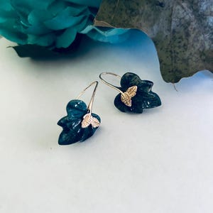 May include: A pair of dark green leaf-shaped earrings with gold accents. The earrings are made of a textured material and have a delicate, feminine design.