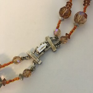 May include: A silver-toned clasp with the word "Vendome" engraved on it. The clasp is attached to a double strand necklace with orange and clear glass beads.