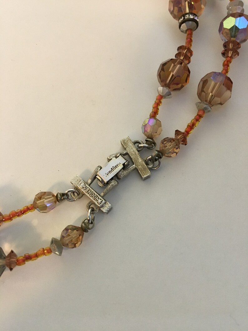 May include: A silver-toned clasp with the word "Vendome" engraved on it. The clasp is attached to a double strand necklace with orange and clear glass beads.