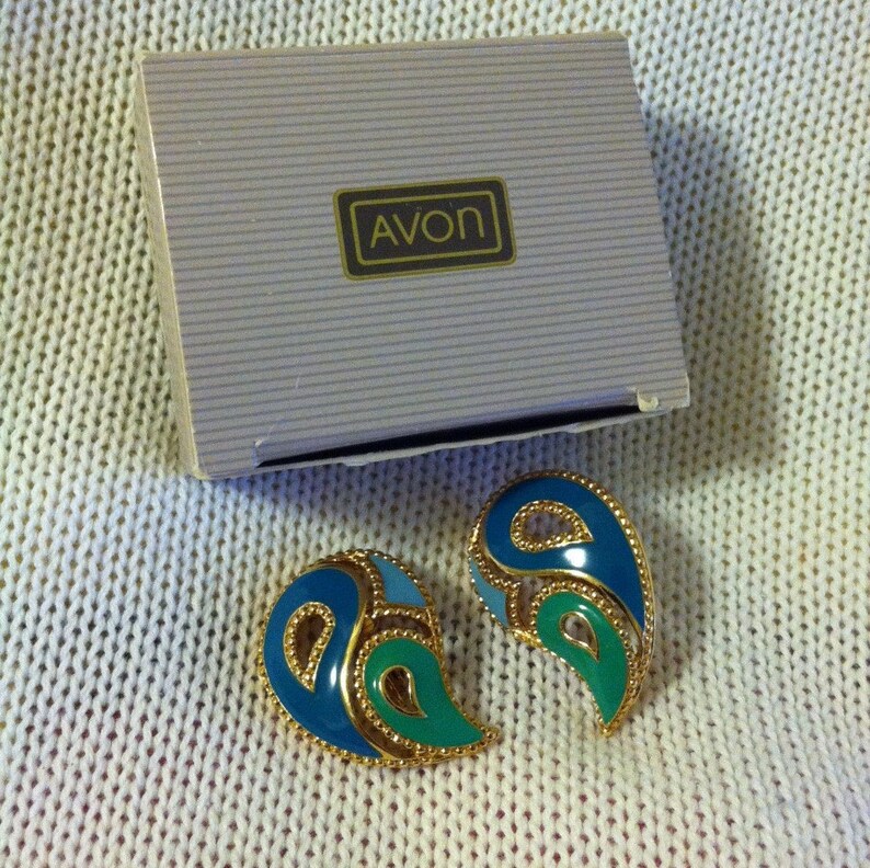May include: A pair of blue and green paisley-shaped earrings with gold trim, in a white box with the word "AVON" printed on it.