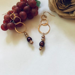 May include: Gold hoop earrings with three interlocking circles and a dangling chain of brown and gold beads.