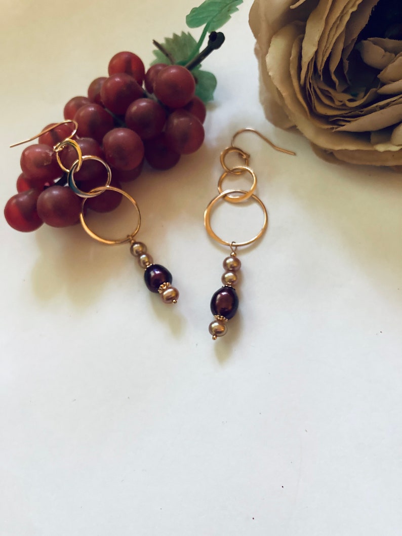 May include: Gold hoop earrings with three interlocking circles and a dangling chain of brown and gold beads.