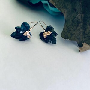 May include: A pair of silver earrings with a green leaf design and gold accents. The leaves are detailed and have a realistic look.