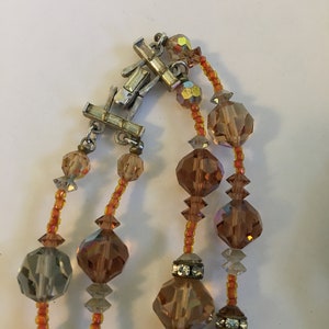 May include: A multi-strand necklace with a silver clasp. The necklace is made of faceted glass beads in shades of brown, gray, and orange.