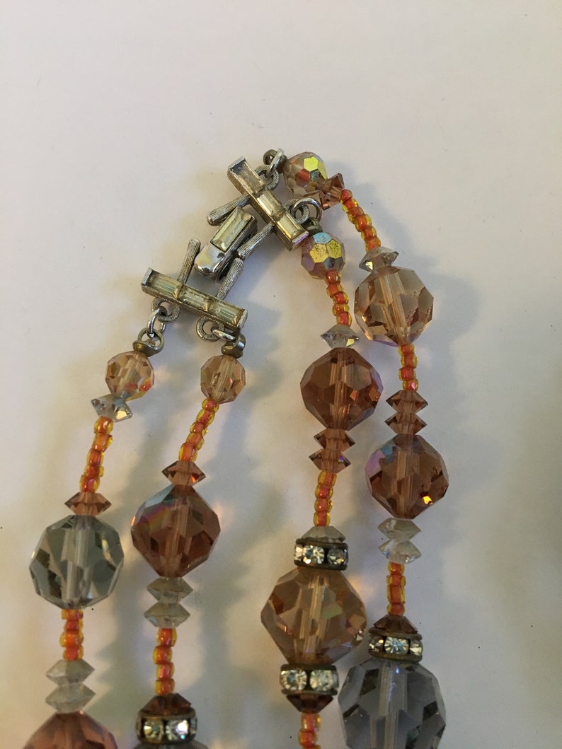 May include: A multi-strand necklace with a silver clasp. The necklace is made of faceted glass beads in shades of brown, gray, and orange.