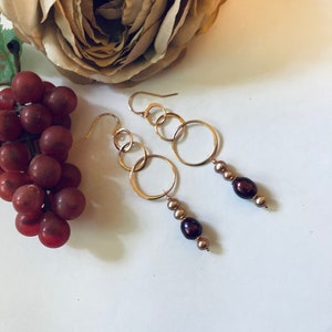 May include: Gold hoop earrings with three connected hoops and a dangling strand of brown pearls.