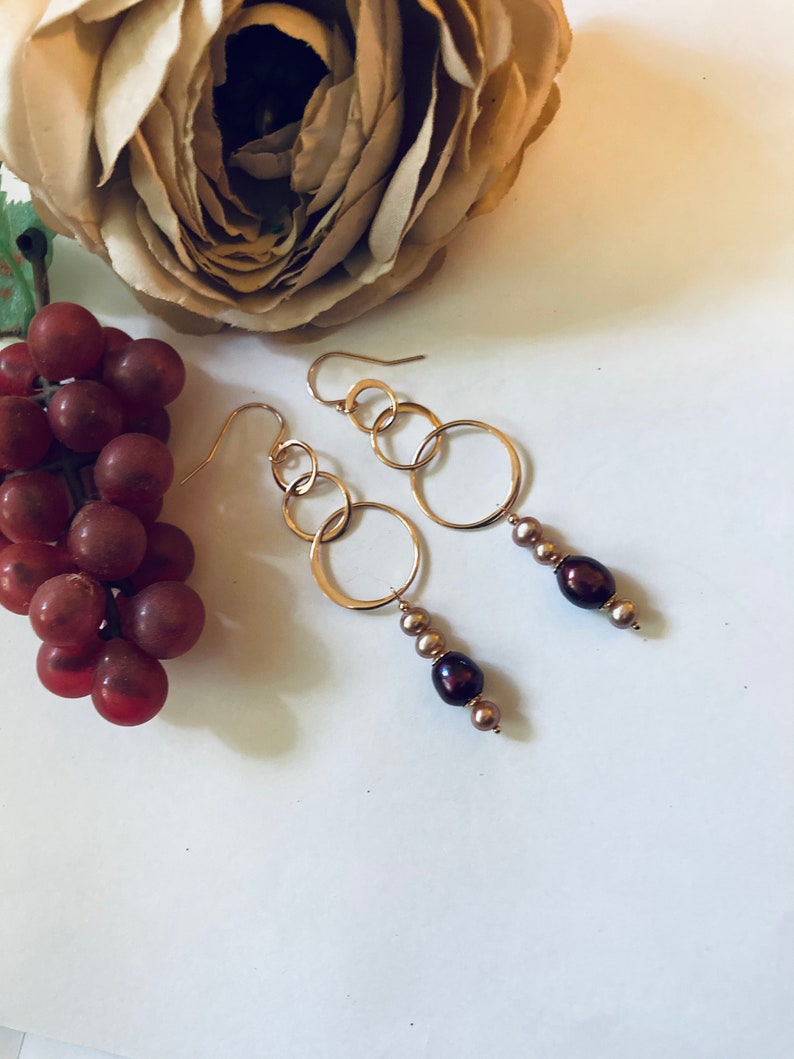 May include: Gold hoop earrings with three connected hoops and a dangling strand of brown pearls.