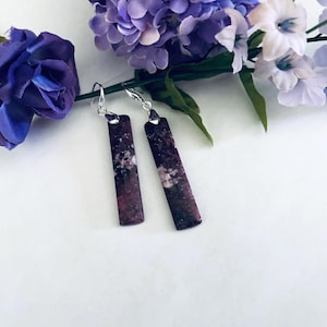 May include: A pair of dangle earrings with silver hooks and rectangular purple and white stone pendants.