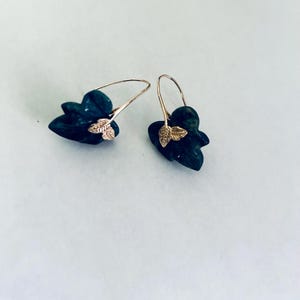 May include: A pair of gold earrings with green gemstone leaves. The leaves are carved and have a textured surface.