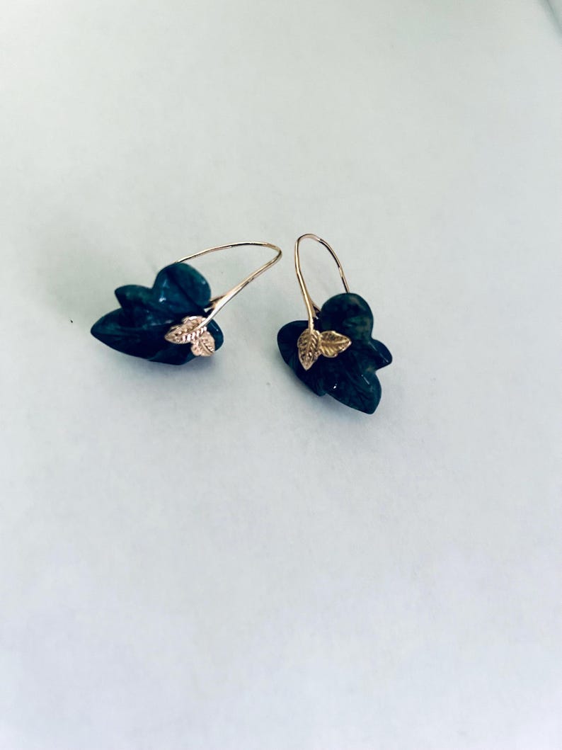 May include: A pair of gold earrings with green gemstone leaves. The leaves are carved and have a textured surface.