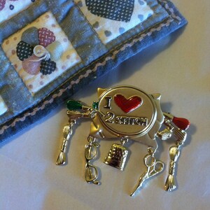 May include: Gold-tone pin with a red heart and the text "I 2 Stitch". The pin has several charms including scissors, a thimble, and spools of thread.