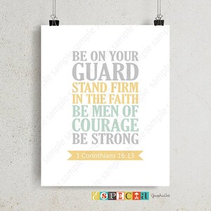 May include: A white poster with the text "BE ON YOUR GUARD, STAND FIRM IN THE FAITH, BE MEN OF COURAGE, BE STRONG" in gray, yellow, and teal. The text "1 Corinthians 16:13" is below. The poster is held by two black binder clips.