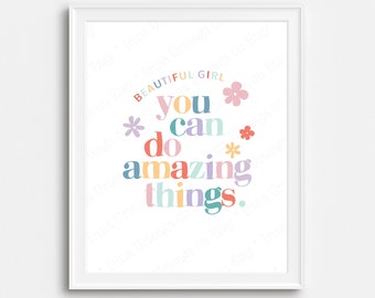 May include: A framed print with the words "BEAUTIFUL GIRL you can do amazing things" in colorful, whimsical lettering. The design includes floral accents in pastel shades, set against a white background.