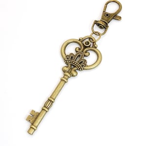 May include: An antique-style key with a decorative design and a lobster clasp. The key is made of a bronze-colored metal and features a detailed crown-like embellishment at the top. The key is approximately 4 inches long.
