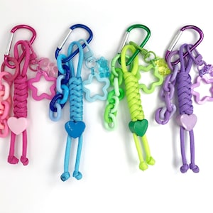 Trending now colorful paracord bag charm keychains with bear and star charms. The rope keychains are made of braided cord and plastic chain links. The colors are pink, blue, green, purple.