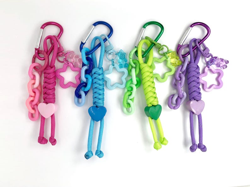 Trending now colorful paracord bag charm keychains with bear and star charms. The rope keychains are made of braided cord and plastic chain links. The colors are pink, blue, green, purple.