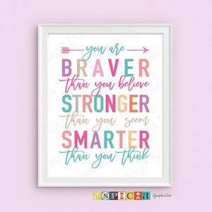 May include: A framed print with a white border features colorful text on a white background. The text reads "You are Braver than you believe, Stronger than you seem, Smarter than you think." The print has a pink background.