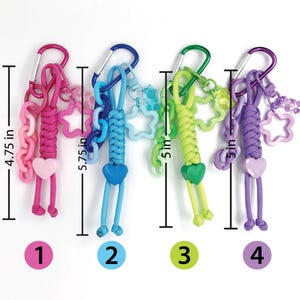 May include: Four colorful keychains with carabiner clips. Each keychain is approximately 4.75 to 5.75 inches long. The keychains feature various charms, including hearts and stars, in pink, blue, green, and purple.