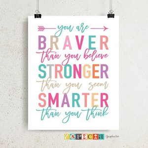May include: A motivational poster with the words "you are BRAVER than you believe, STRONGER than you seem, SMARTER than you think" in various colorful fonts. The poster is held by two black binder clips.
