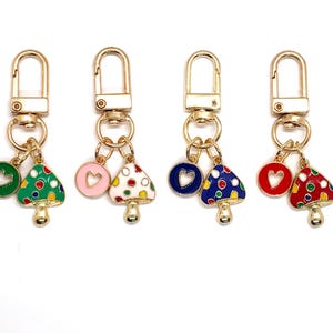 May include: Four gold keychains with mushroom and heart charms. Each keychain has a different colored mushroom charm with white polka dots and a heart charm in a matching color. The colors are green, pink, blue, and red.