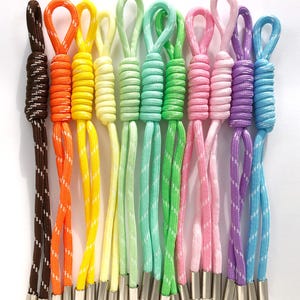 May include: A collection of colorful drawstring cords with metal tips. The cords are in various colors, including brown, orange, yellow, green, pink, purple, and blue. Each cord has a loop at the top.
