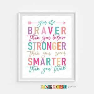 May include: A framed print with the words "You are Braver Than you believe, Stronger Than you seem, Smarter Than you think" in colorful text. The print has a white border and a white background. The bottom right corner has the text "& SPECIAL GraphicArt".