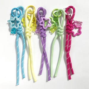May include: Five colorful keychains with star-shaped charms and coordinating rope. The keychains feature a variety of colors, including blue, yellow, purple, green, and pink. Each keychain has a metal clasp.