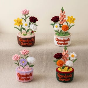 Puede incluir: Cuatro arreglos florales de ganchillo hechos a mano en macetas pequeñas. Cada maceta tiene el texto "Grandma's Garden". Las flores incluyen narcisos, rosas, margaritas y otras flores coloridas. Las macetas son marrones, blancas, rosas y verdes.
