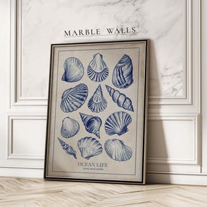 May include: Framed print featuring blue seashell illustrations on a beige background. The artwork includes the text "MARBLE WALLS" at the top and "OCEAN LIFE" at the bottom. The frame is black, and the print is displayed against a marble wall.