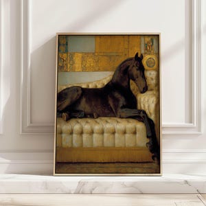 May include: A framed artwork shows a dark brown horse resting on a cream-coloured, buttoned sofa. The background has gold and blue geometric patterns. The artwork is displayed on a white surface against a white wall.