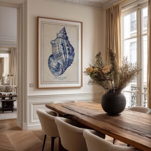 Coastal-inspired seashell wall art print in navy tones on aged beige paper, framed above a wooden dining table in an elegant dining room.