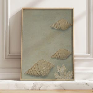 May include: A framed artwork featuring three textured seashells in shades of beige and tan against a muted green background. A white coral-like element is at the bottom. The artwork is in a light brown wooden frame.