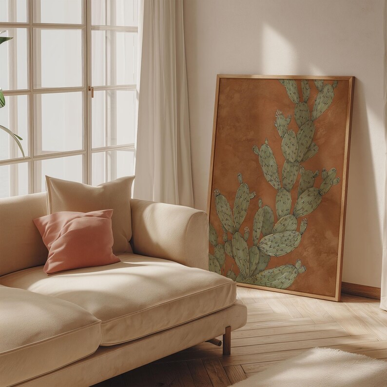 Vintage prickly pear cactus artwork in sage green and terracotta, quiet desert mood, styled as a framed art print leaning by a sofa in late sun.