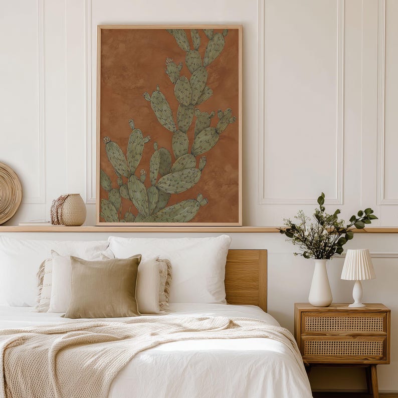 Desert prickly pear illustration in terracotta and sage green, vintage-line style and serene feel, displayed as a framed wall art print above a bed.
