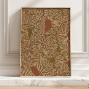 May include: A framed art print featuring a repeating pattern of stylized, fan-like shapes in shades of brown and gold against a terracotta background. The artwork is displayed in a light-colored wooden frame, adding a touch of warmth.