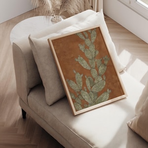 Rustic prickly pear cactus in green and terracotta, vintage desert mood, displayed as a framed wall art print resting on a cushioned chair.