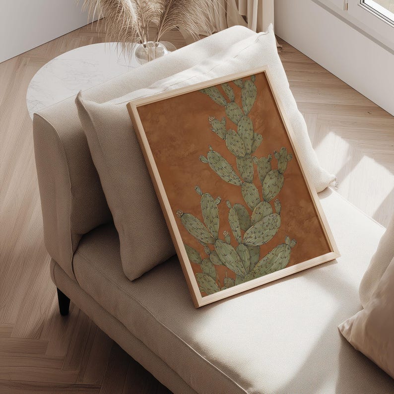 Rustic prickly pear cactus in green and terracotta, vintage desert mood, displayed as a framed wall art print resting on a cushioned chair.